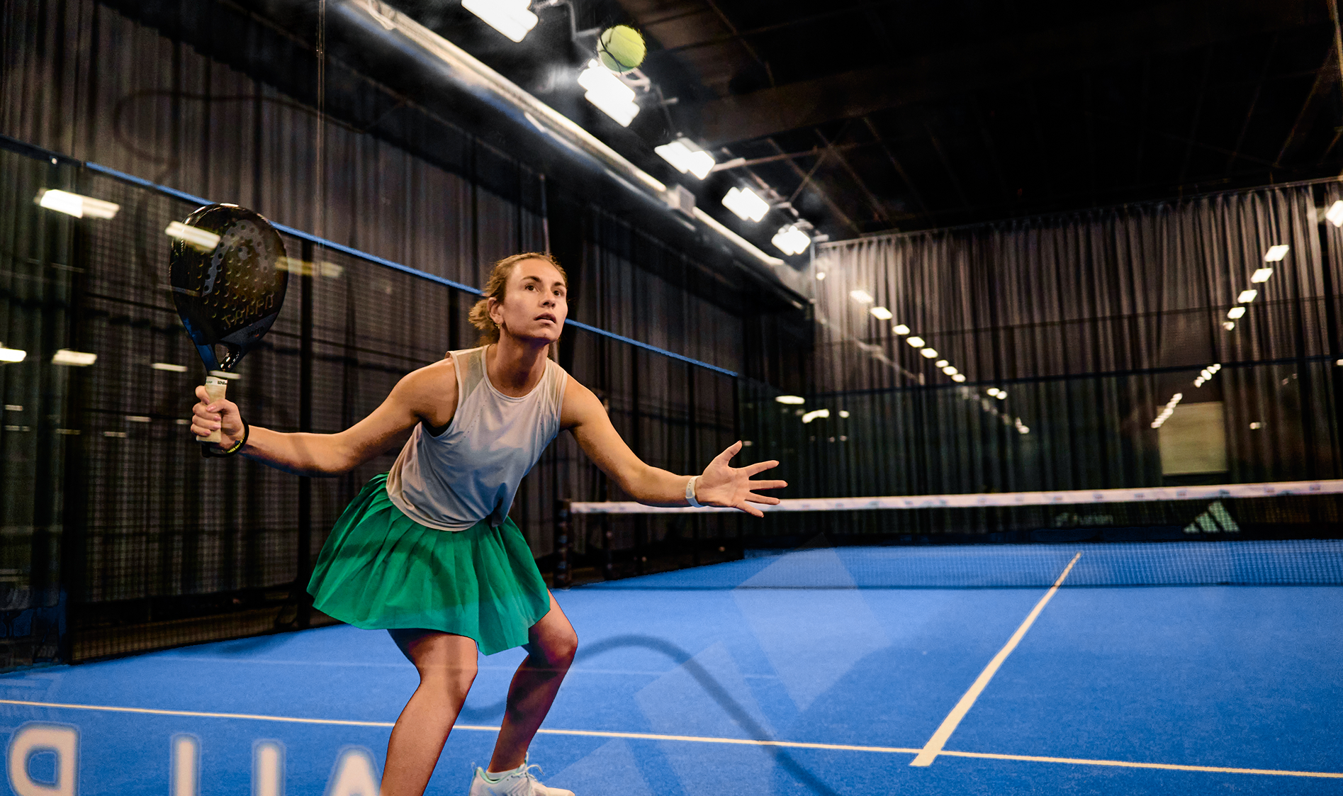 Woman playing padel on an indoor court with a blue floor.